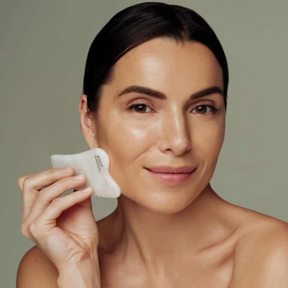 Woman holding White gua sha stone by Pari Satiss close to here face