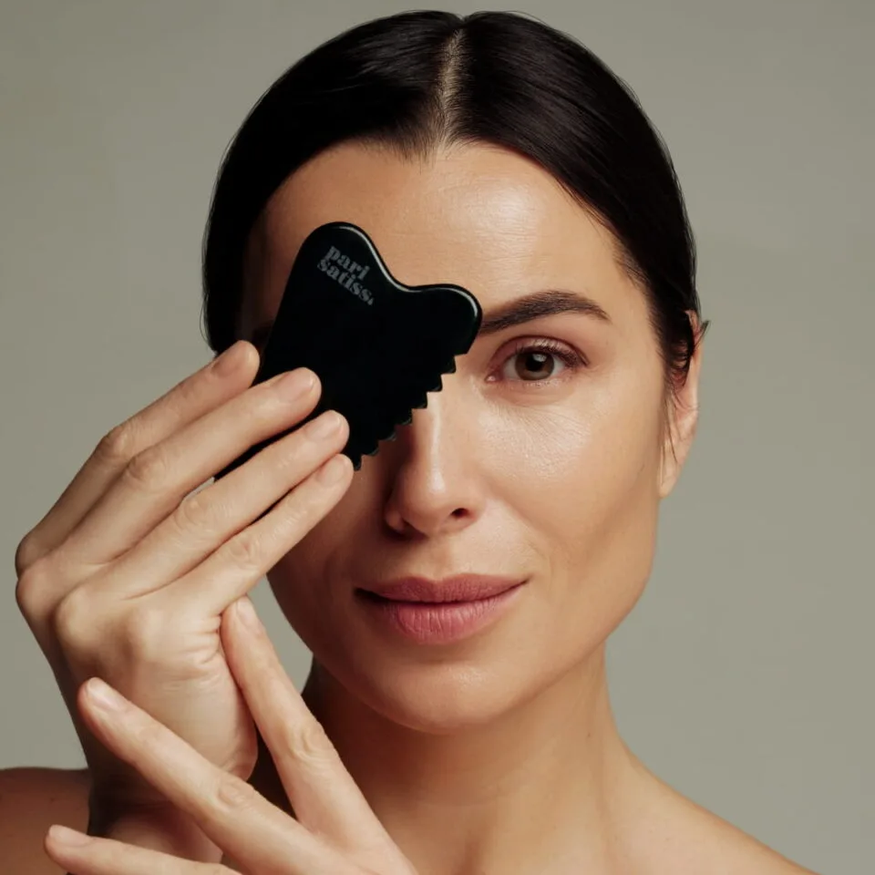 Woman holding Green gua sha stone by Pari Satiss close to here face
