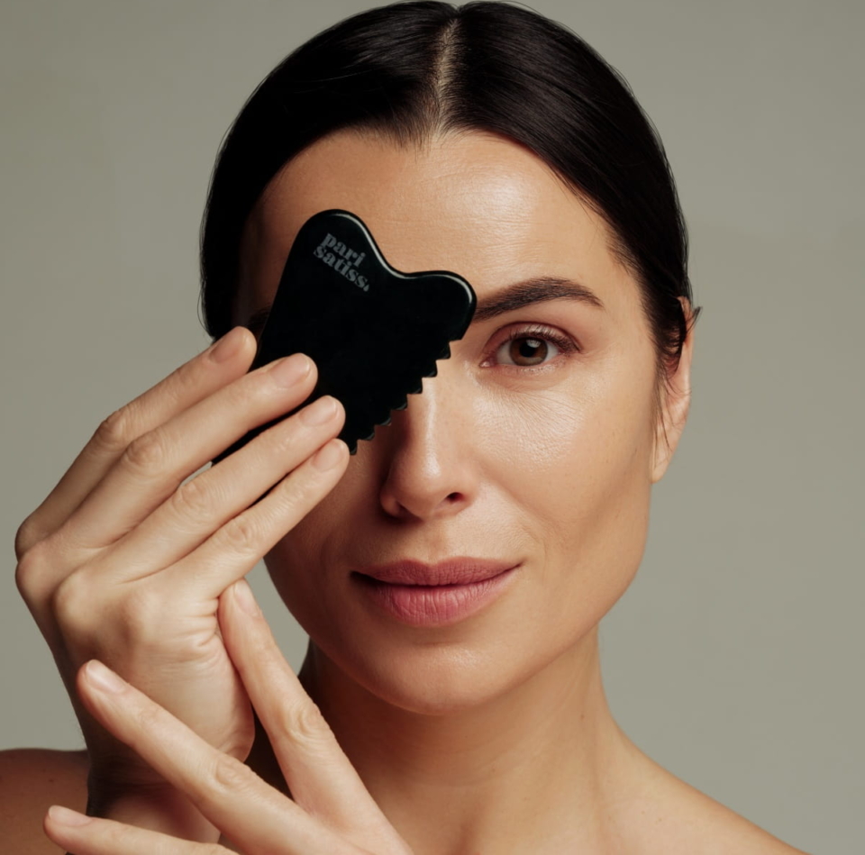 Woman holding Green gua sha stone by Pari Satiss close to here face