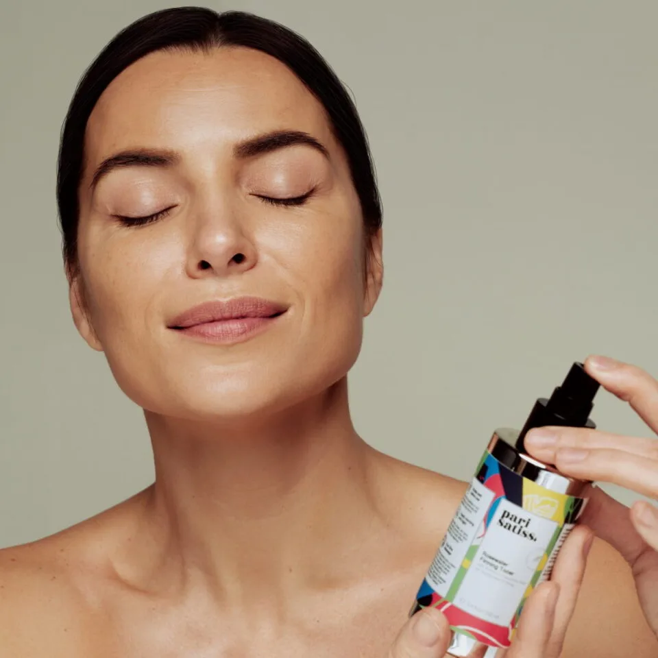 Woman holding bottle with Rosewater Firming Toner by Pari Satiss close to here face
